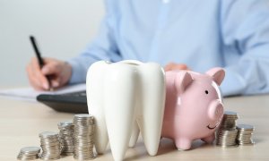 A ceramic model of a tooth, a piggy bank, and coins on a wooden table