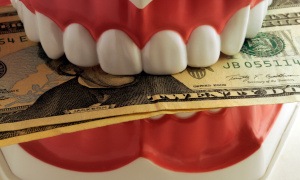 A 3D illustration of a jaw model biting dollar bills